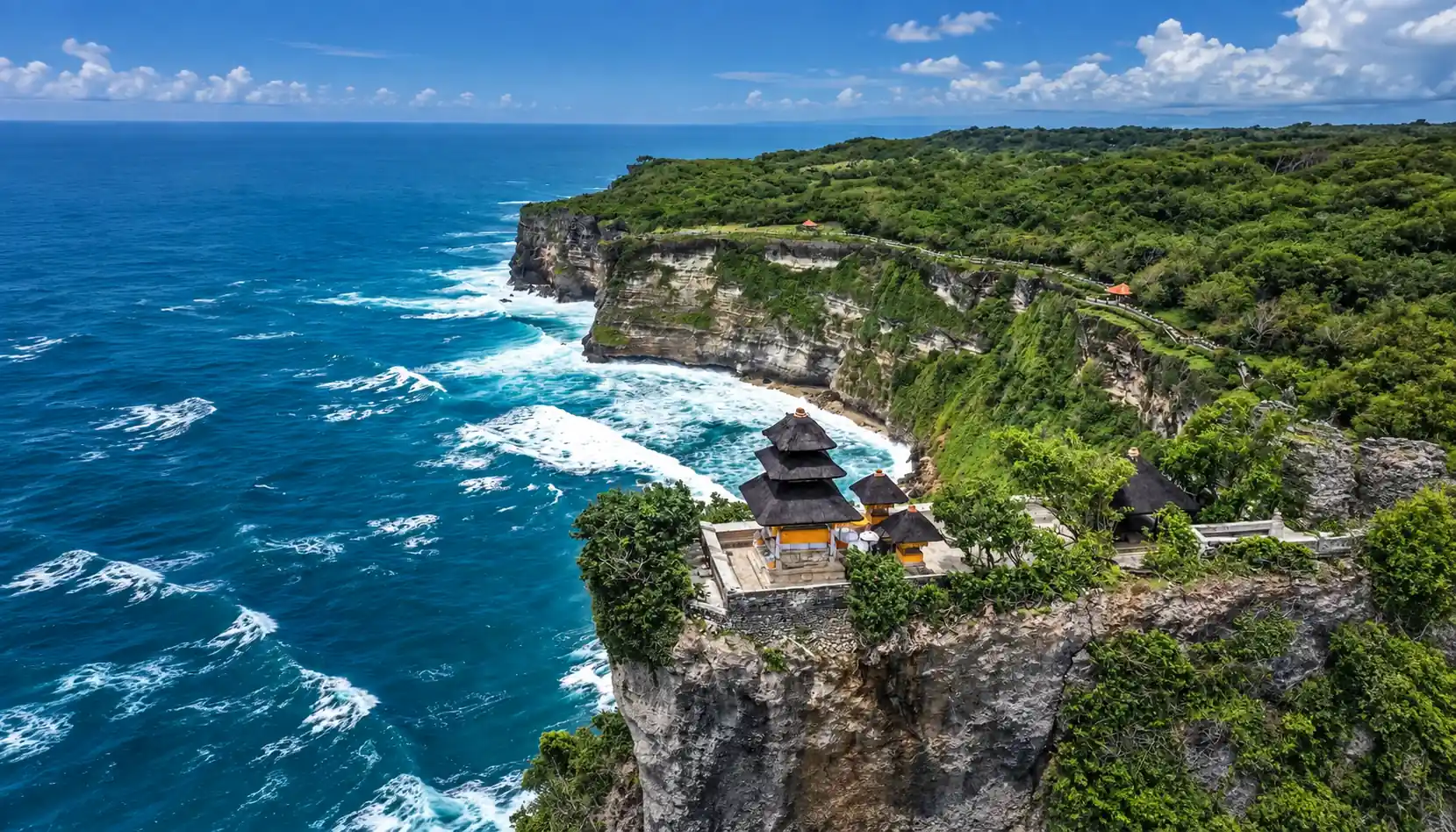 Uluwatu Temple on a limestone cliff overlooking the blue Indian Ocean and green coastline